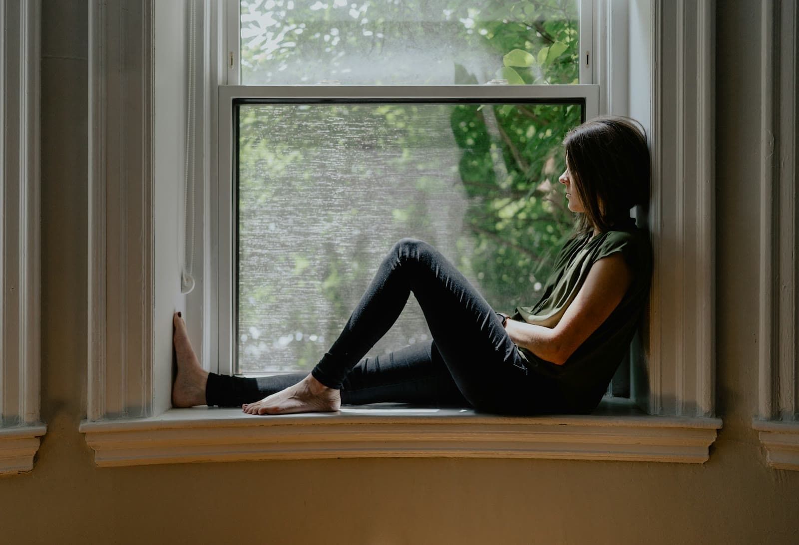A woman resting on a window seat, gazing outside