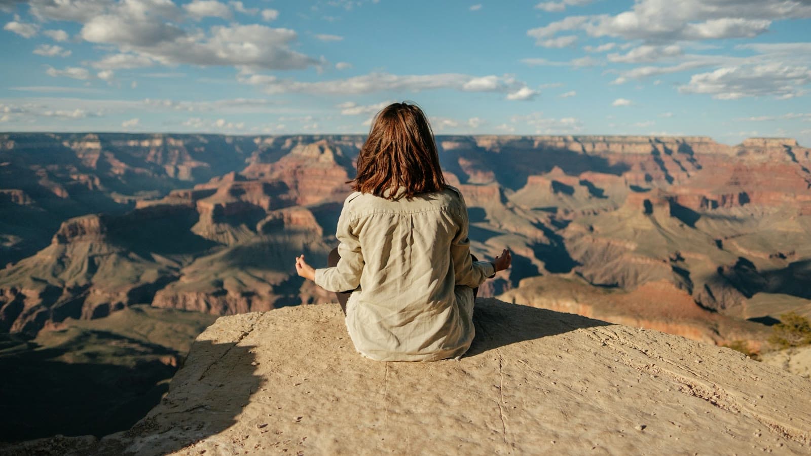 A woman meditating on a clifftop above the Grand Canyon